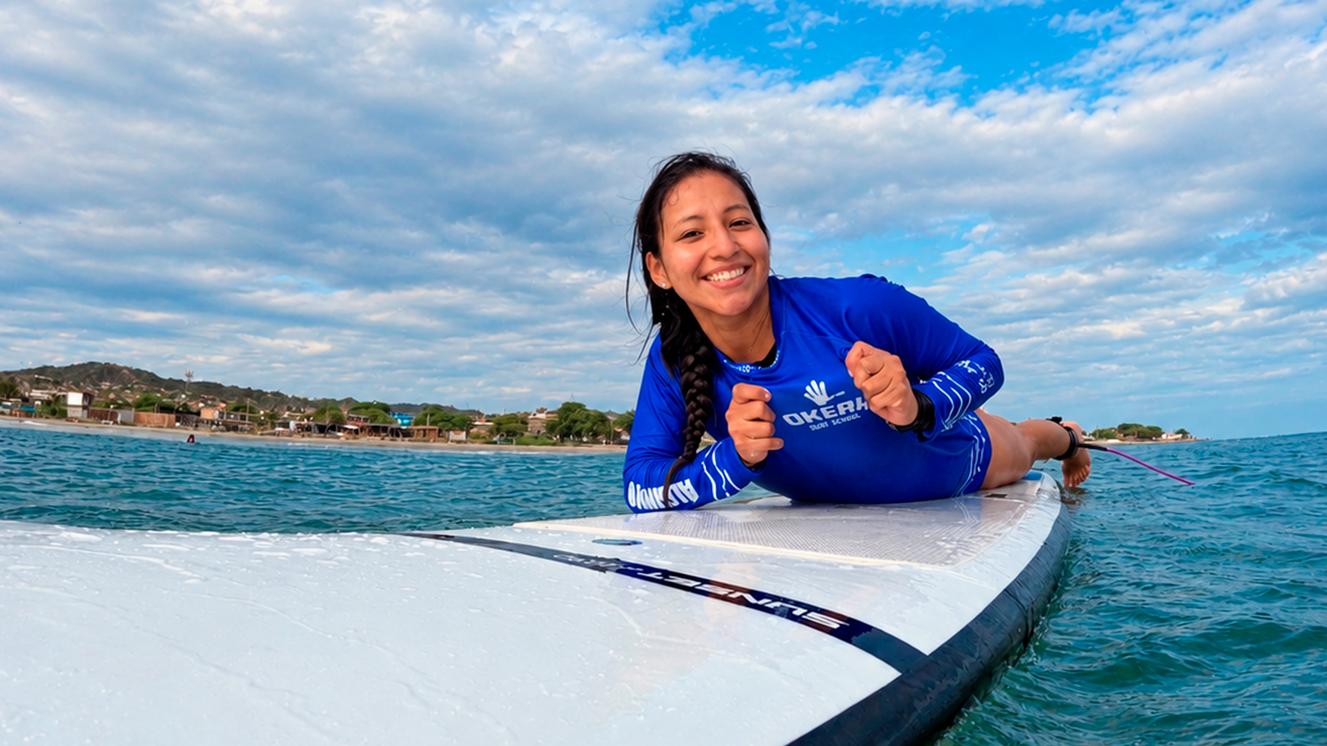 Alumna sonriendo sobre una tabla de surf en el mar